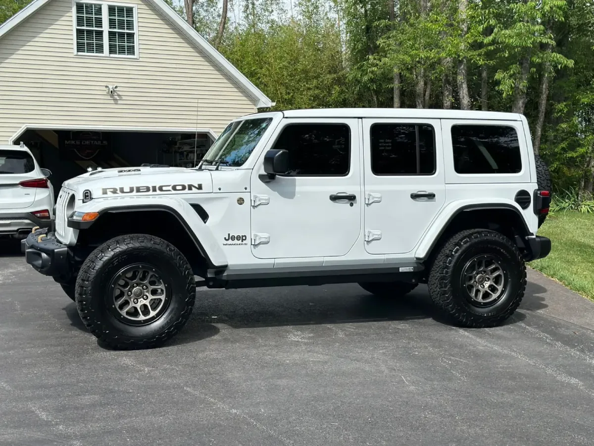 A Jeep Wrangler Rubicon with large off-road tires, parked in a driveway with a clean, glossy finish.