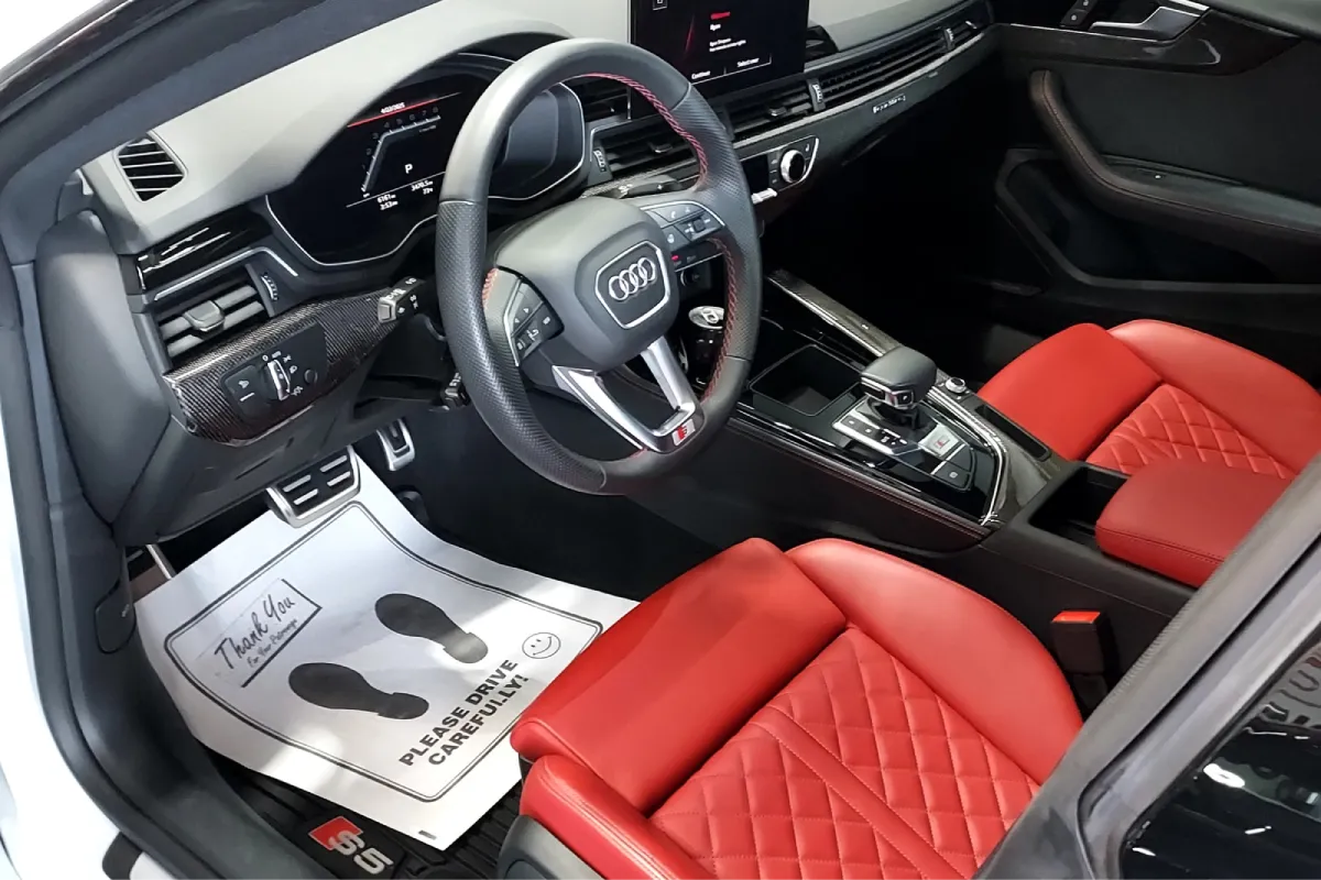 The interior of an Audi S5, showcasing red leather seats and a sleek dashboard with a black steering wheel.