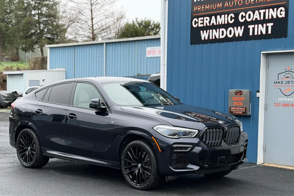 Front angle of black BMW X6 in front of a blue building with shiny exterior