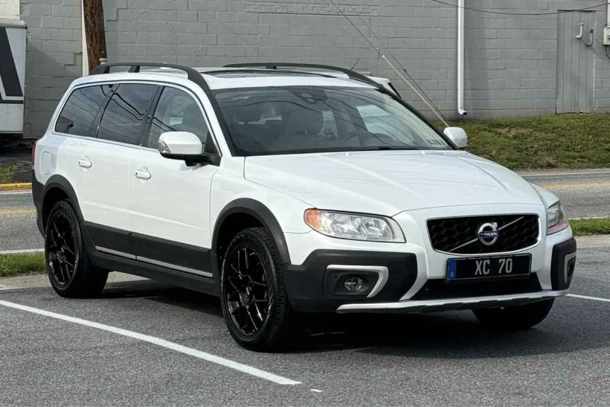 Front view of a white Volvo XC70 with black wheels in a parking lot.