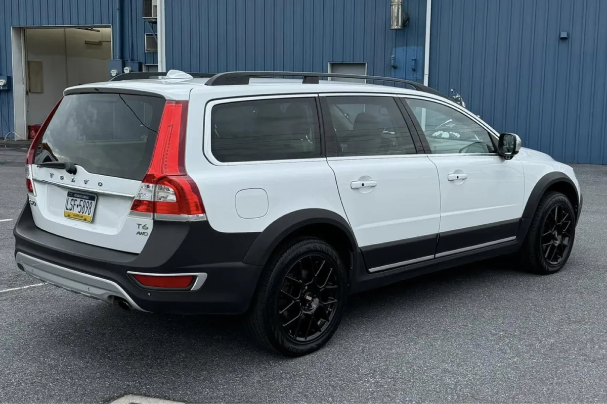 White Volvo XC70 with black wheels parked outside a building.