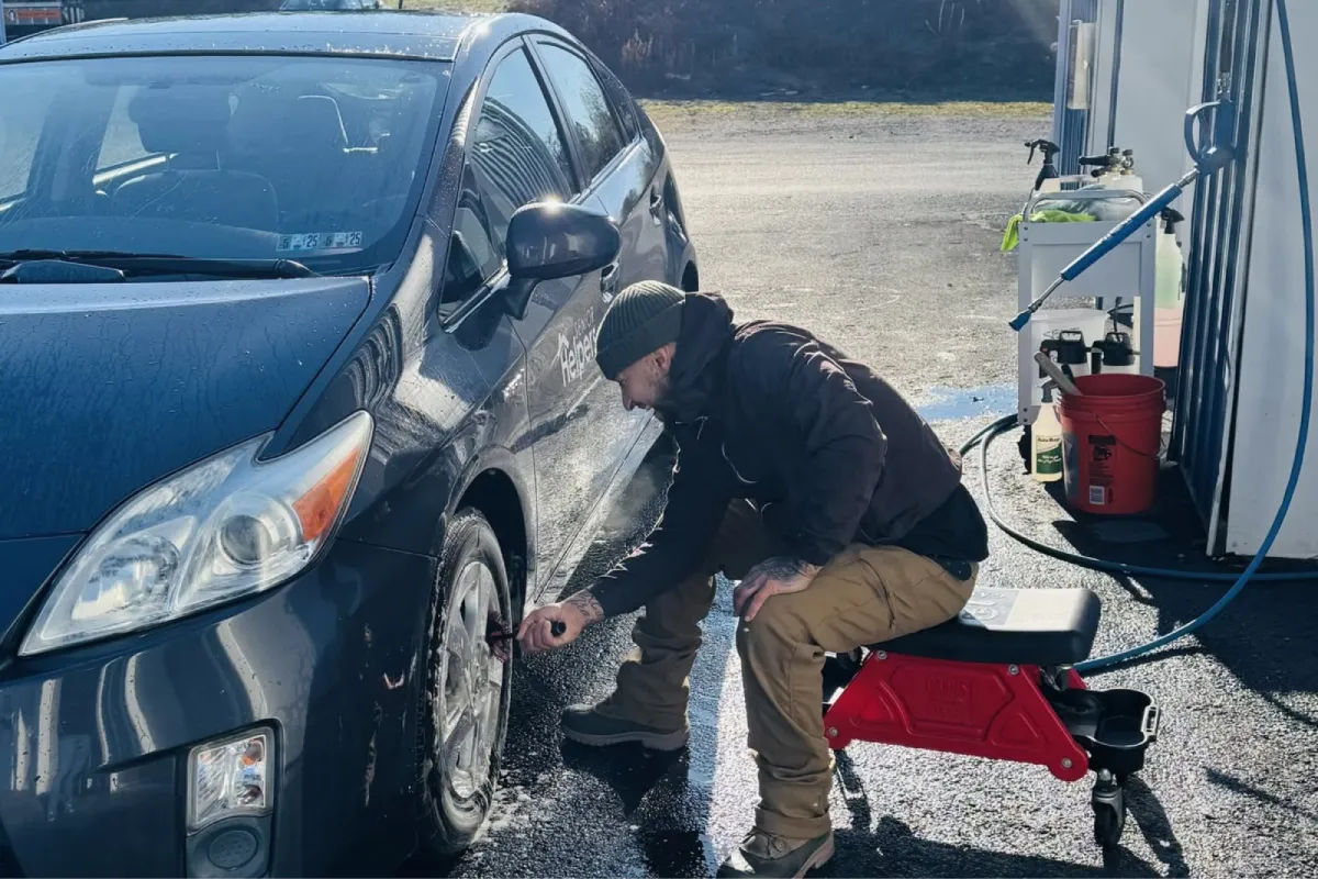 Detailer cleaning the wheel of a blue car.